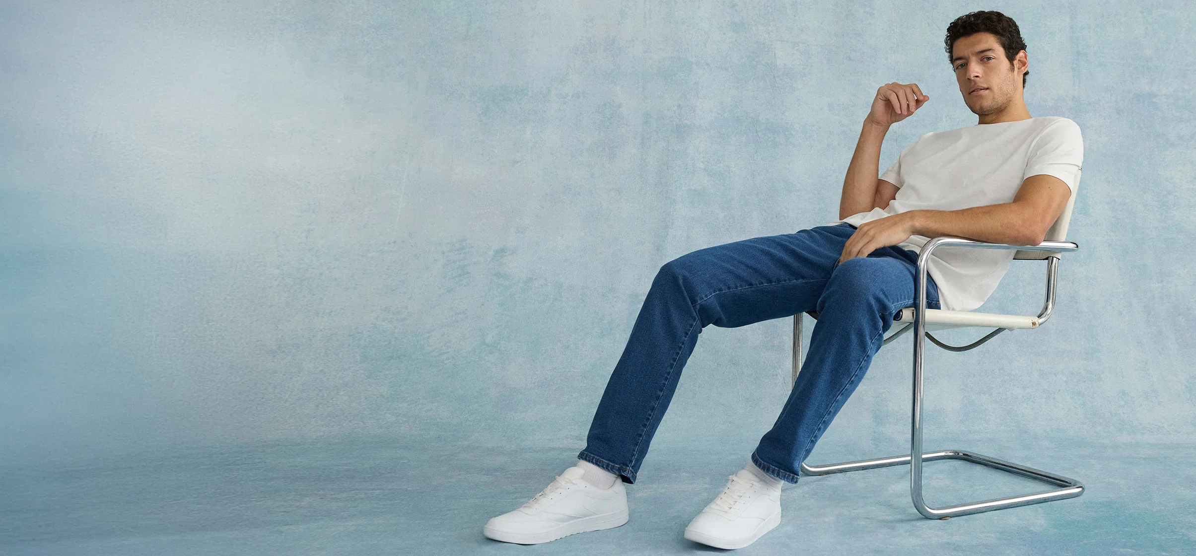 Look relaxat: tricou alb, blugi albaștri și sneakeri albi pe un scaun modern.