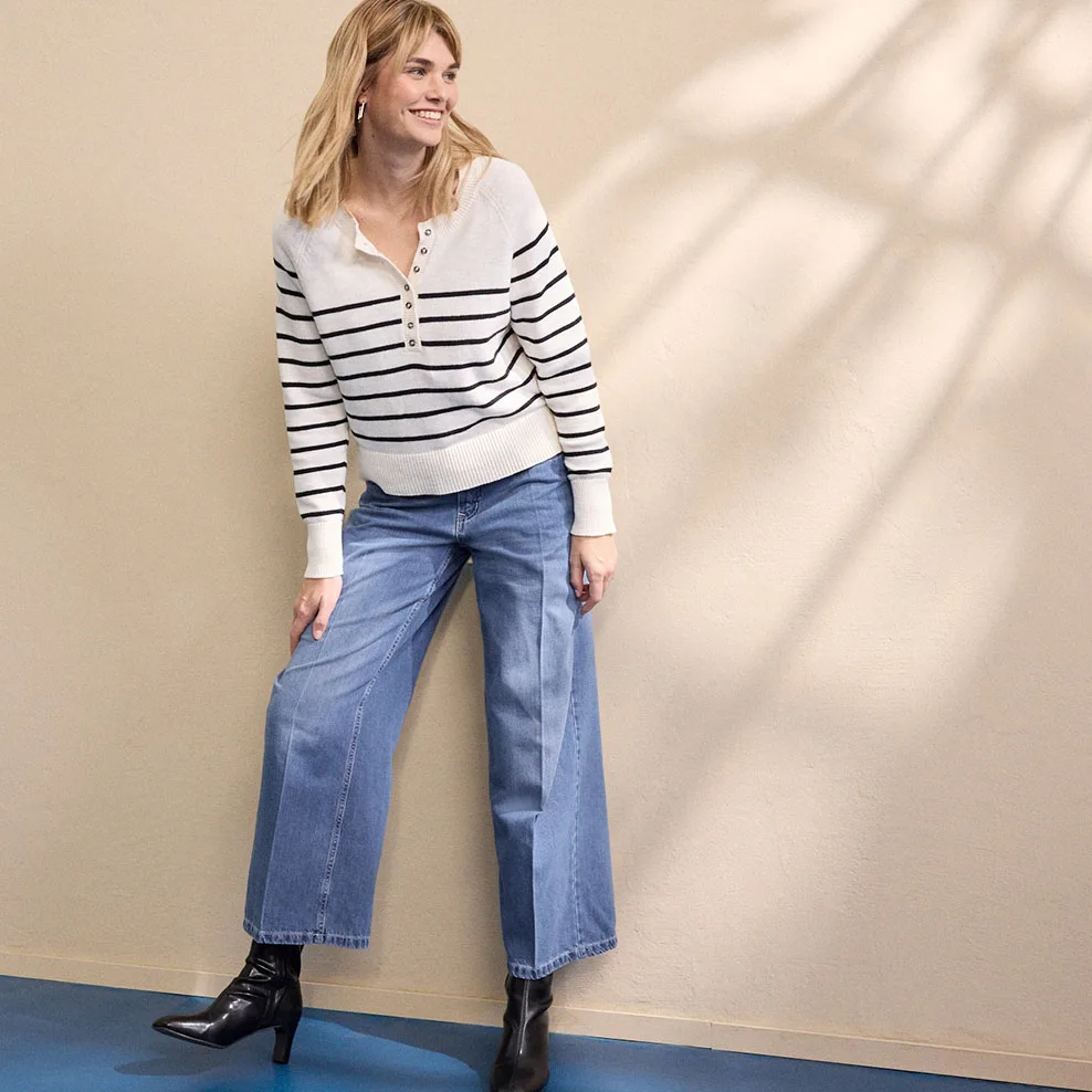 Pulover alb cu dungi, cu fermoar, combinat cu blugi largi și cizme negre.