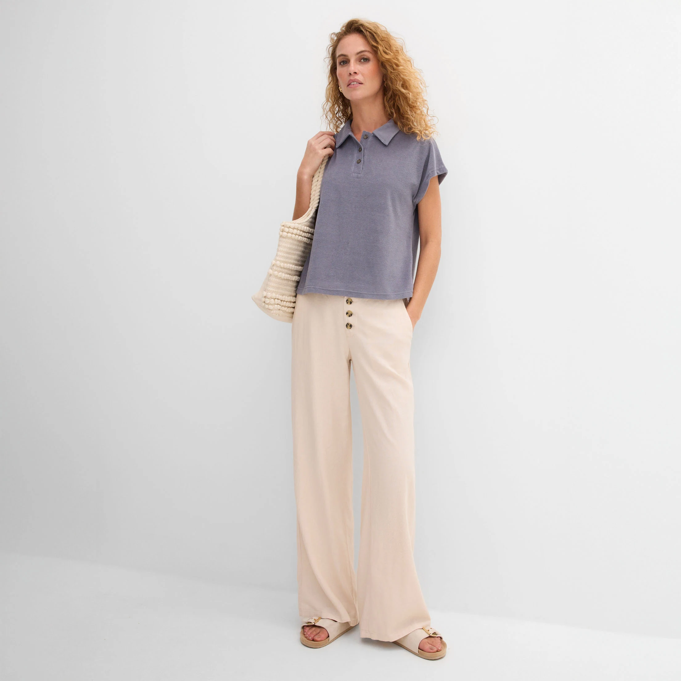 Femeie elegantă care poartă un tricou albastru lejer și pantaloni largi bej.
