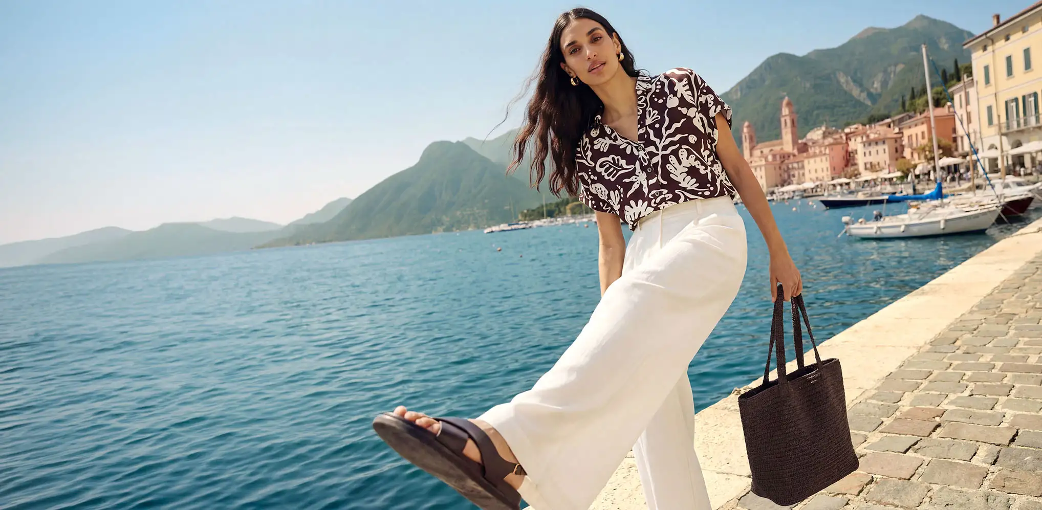 Femeie în port, cu pantaloni albi și tricou maro cu model.